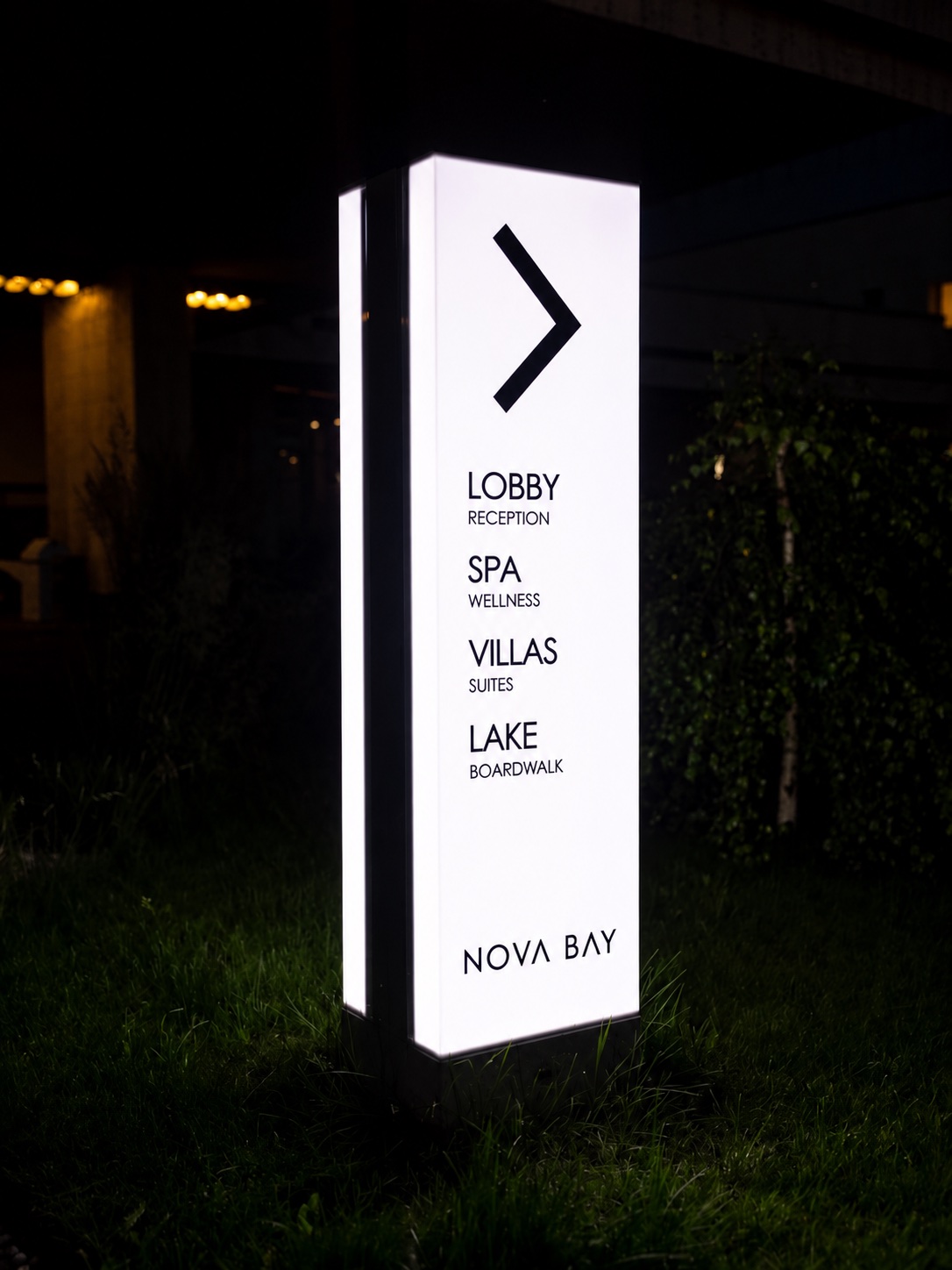 Illuminated wayfinding pylon in a landscaped hospitality setting.